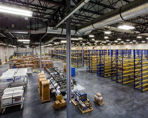 Interior of large warehouse. Empty shelving racks occupy half the room. Boxes of supplies are on pallets on the floor occupy the other half of the room.